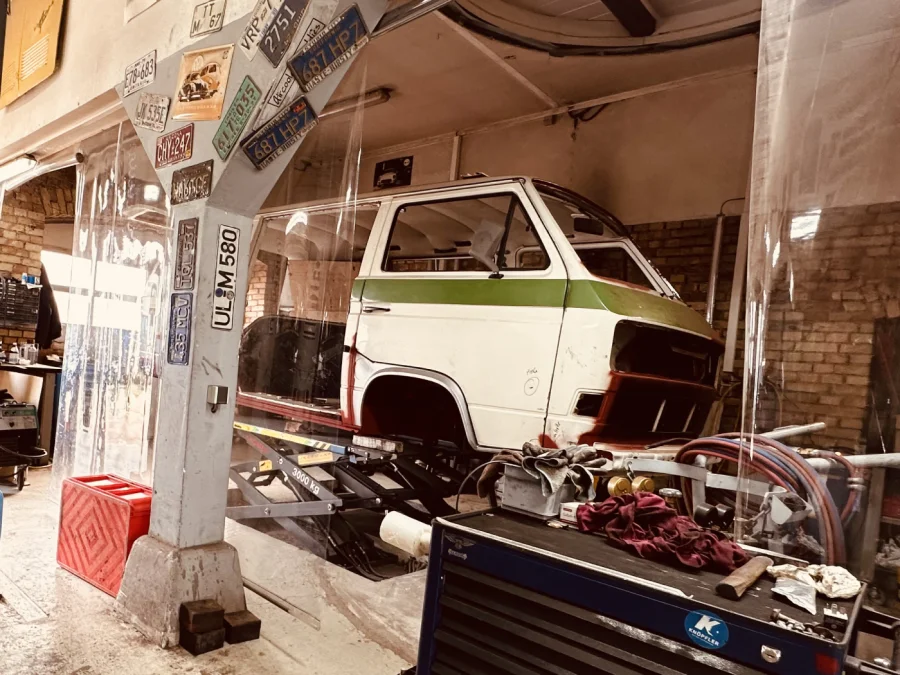 Klassischer Campervan auf einer Hebebühne mit sichtbarem Reifen und Fahrwerk in einer Werkstatt